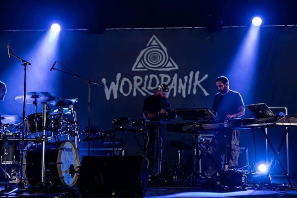 World Panik sur scène sous une lumière bleue, le logo du groupe en fond